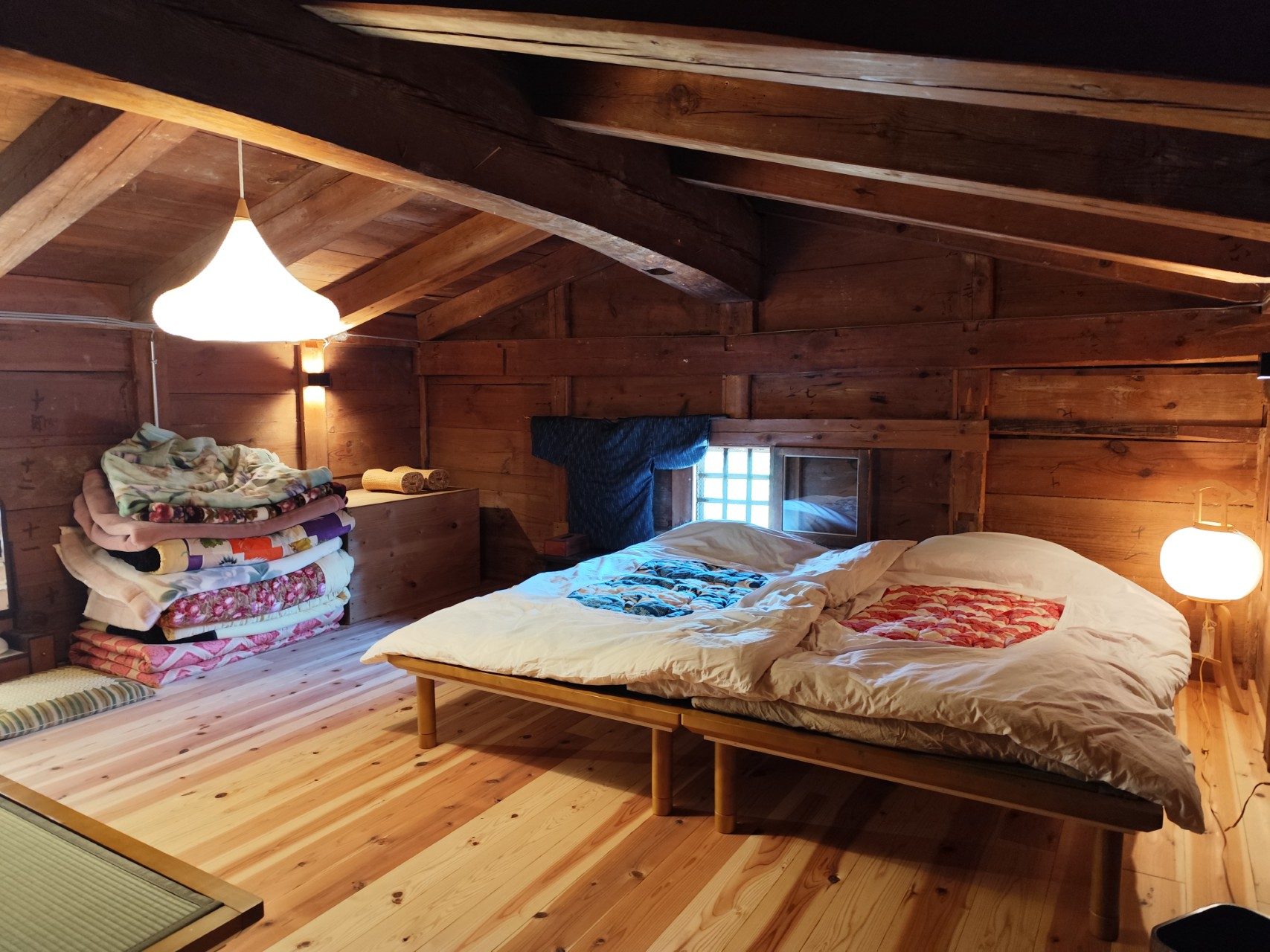 Two wooden beds made up in the loft, with a kimono at the window